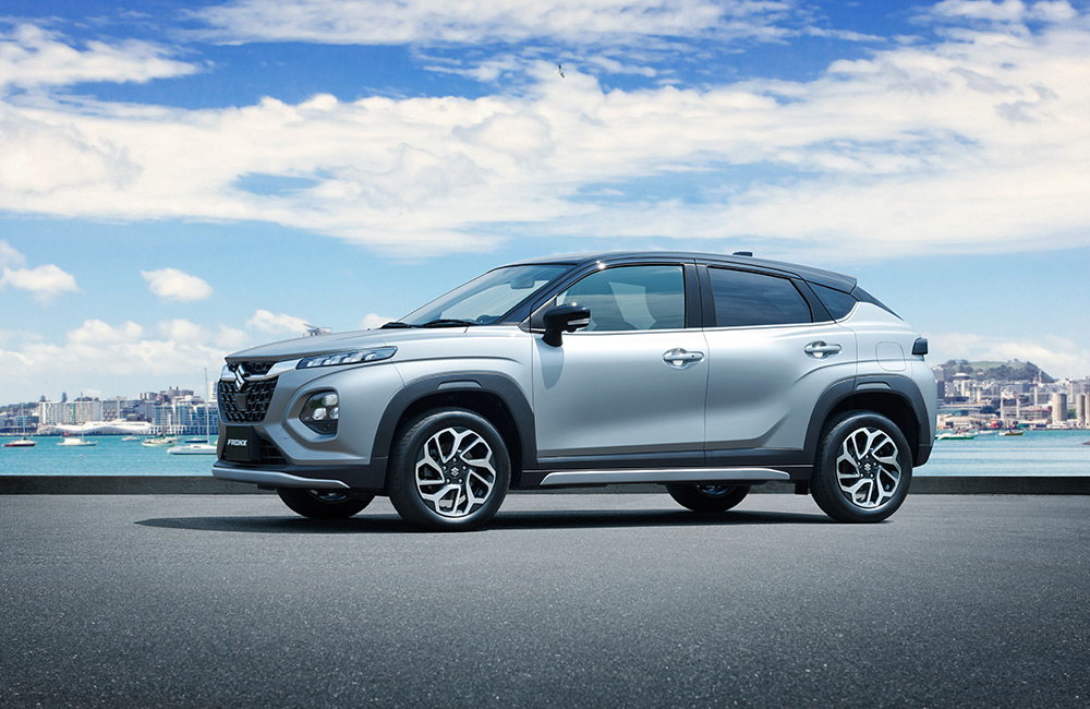 Side angle of a silver Suzuki Fronx parked on a waterfront street