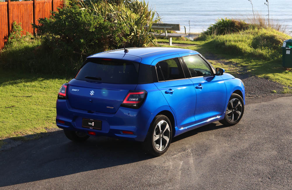 Blue Swift with black roof driving on a forest road